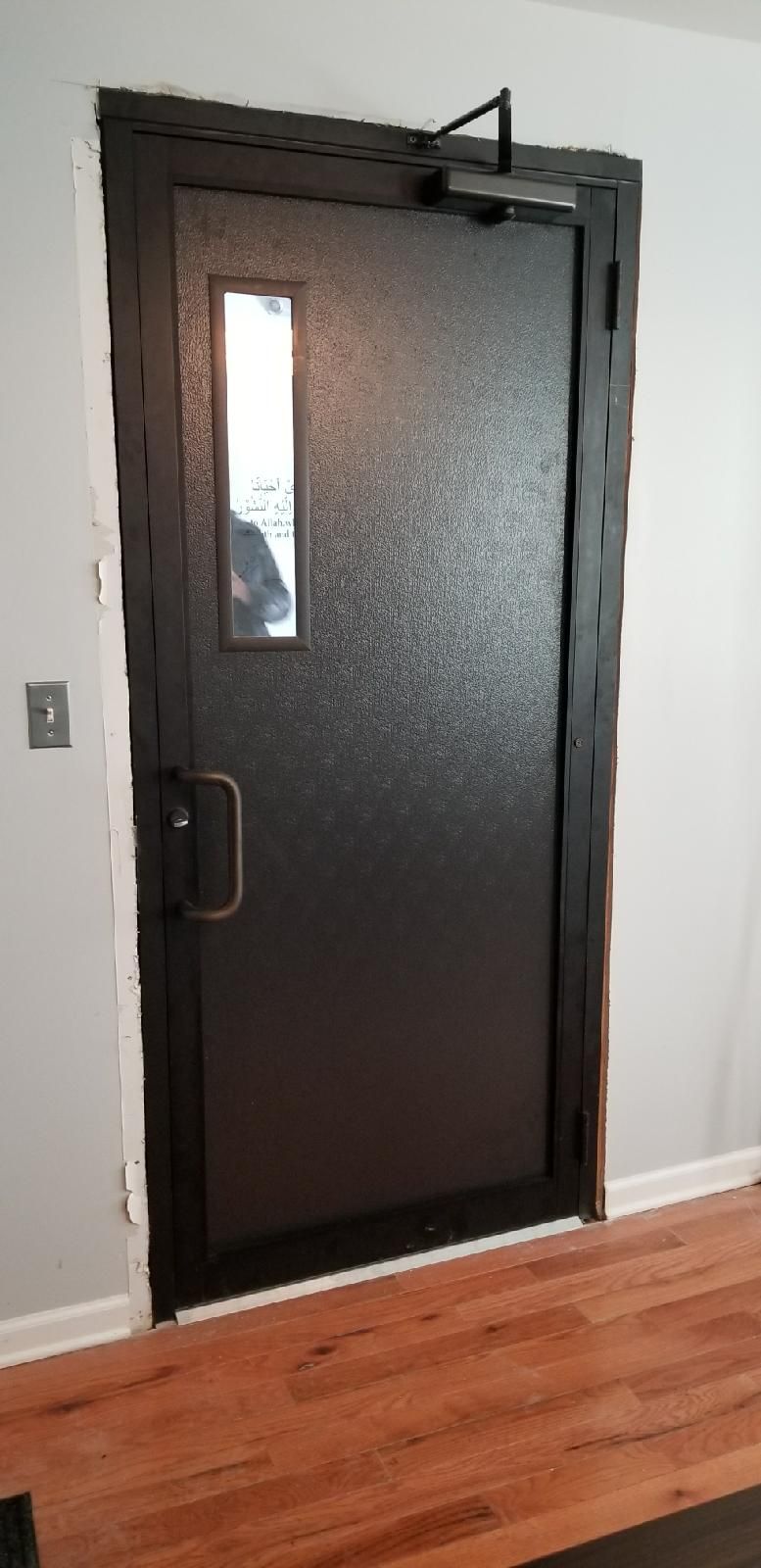 A black door with a window in a room with hardwood floors.