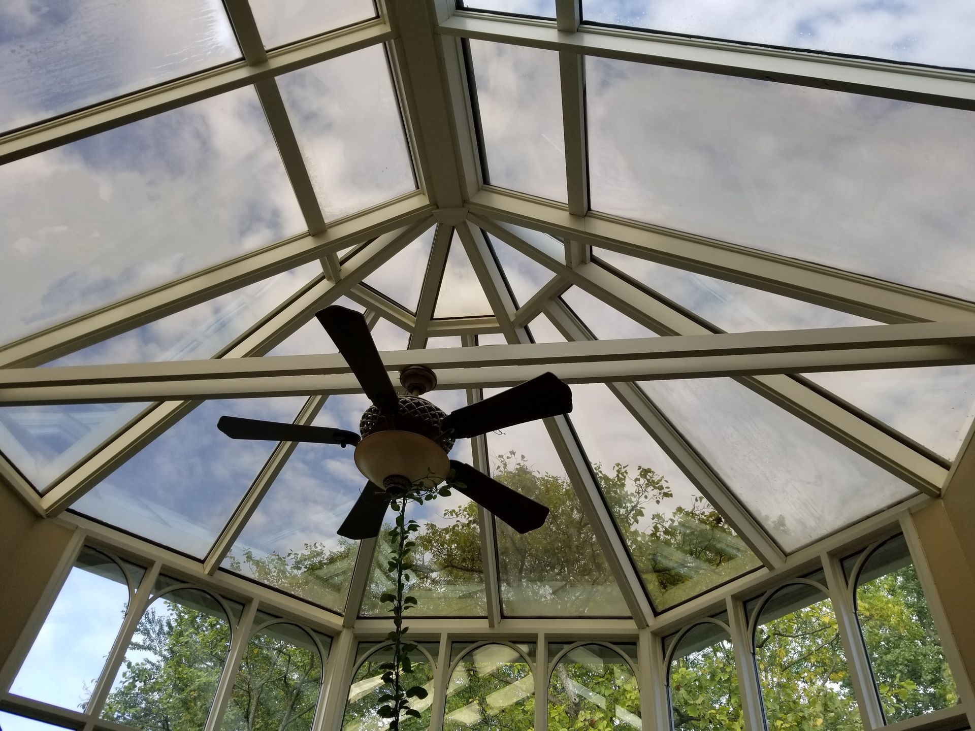 A ceiling fan is hanging from the ceiling of a glass room.