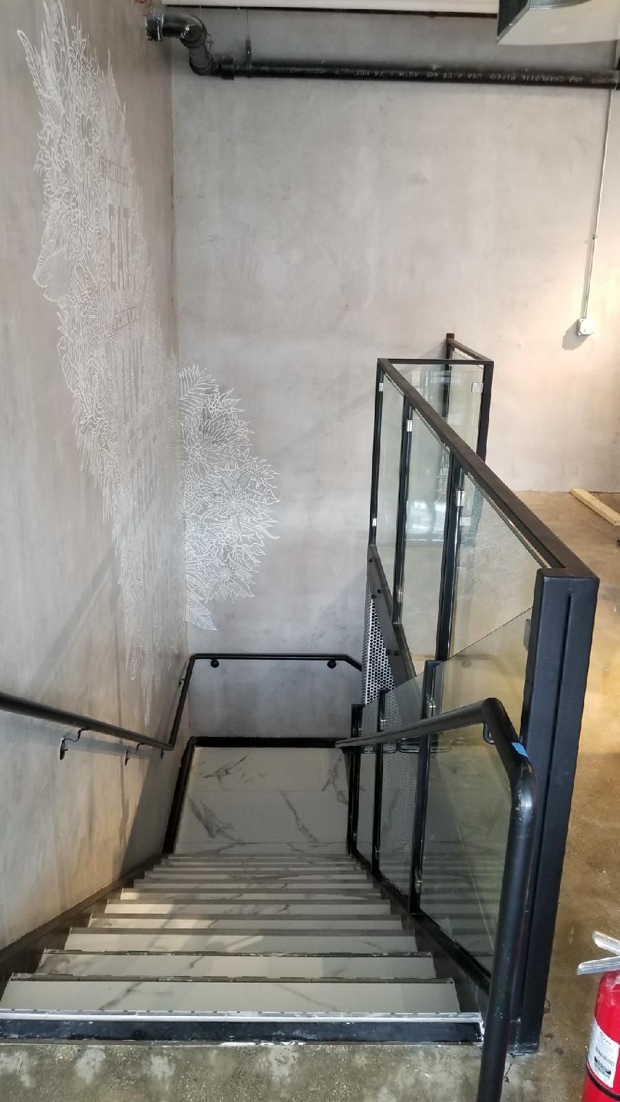 A set of stairs with a glass railing and a fire extinguisher.