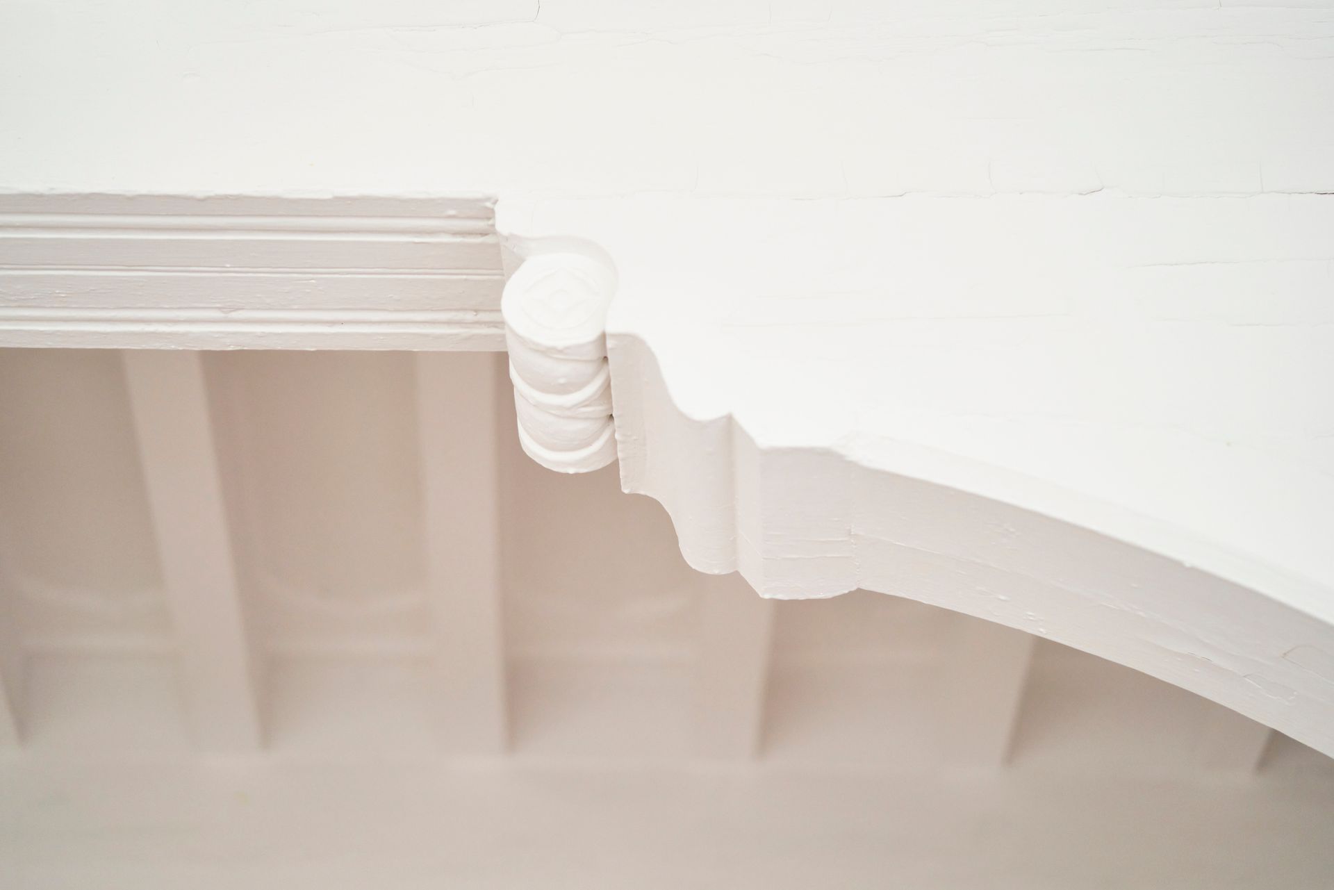 White architectural detail of a curved ceiling or arch with decorative molding, and a cylindrical accent.