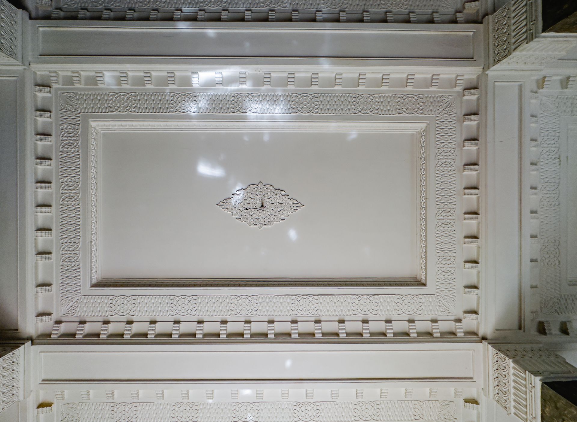 White ornate ceiling with geometric patterns and central floral design.