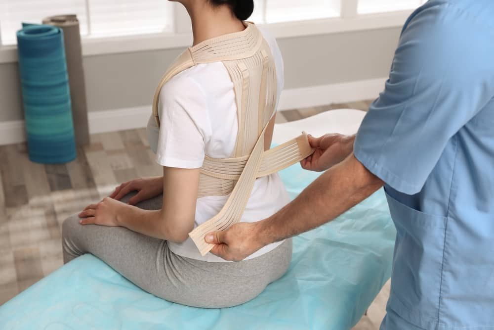 A Man is Putting a Posture Corrector on a Woman 's Back — Sugarland Chiropractic Centre in Avoca, QLD