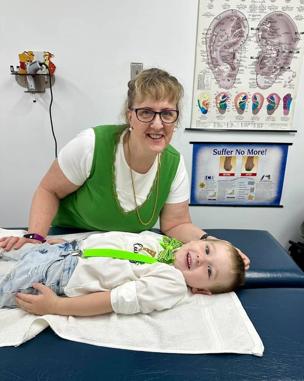 A Woman is Sitting Next to a Young Boy Laying on a Table — Sugarland Chiropractic Centre in Avoca, QLD