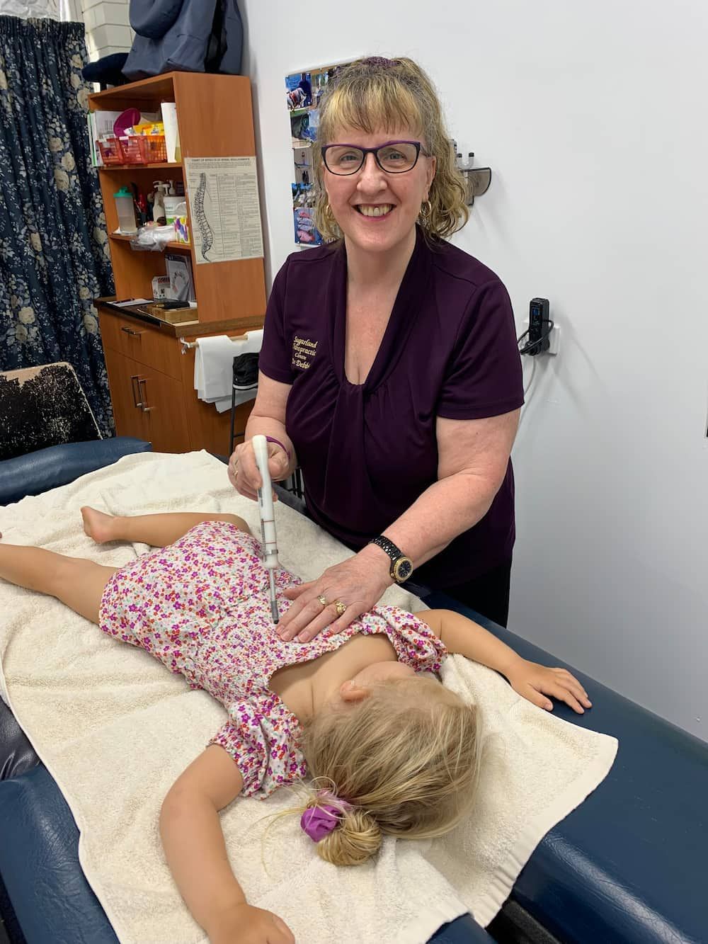 A Woman is Examining a Little Girl Laying on a Table — Sugarland Chiropractic Centre in Avoca, QLD