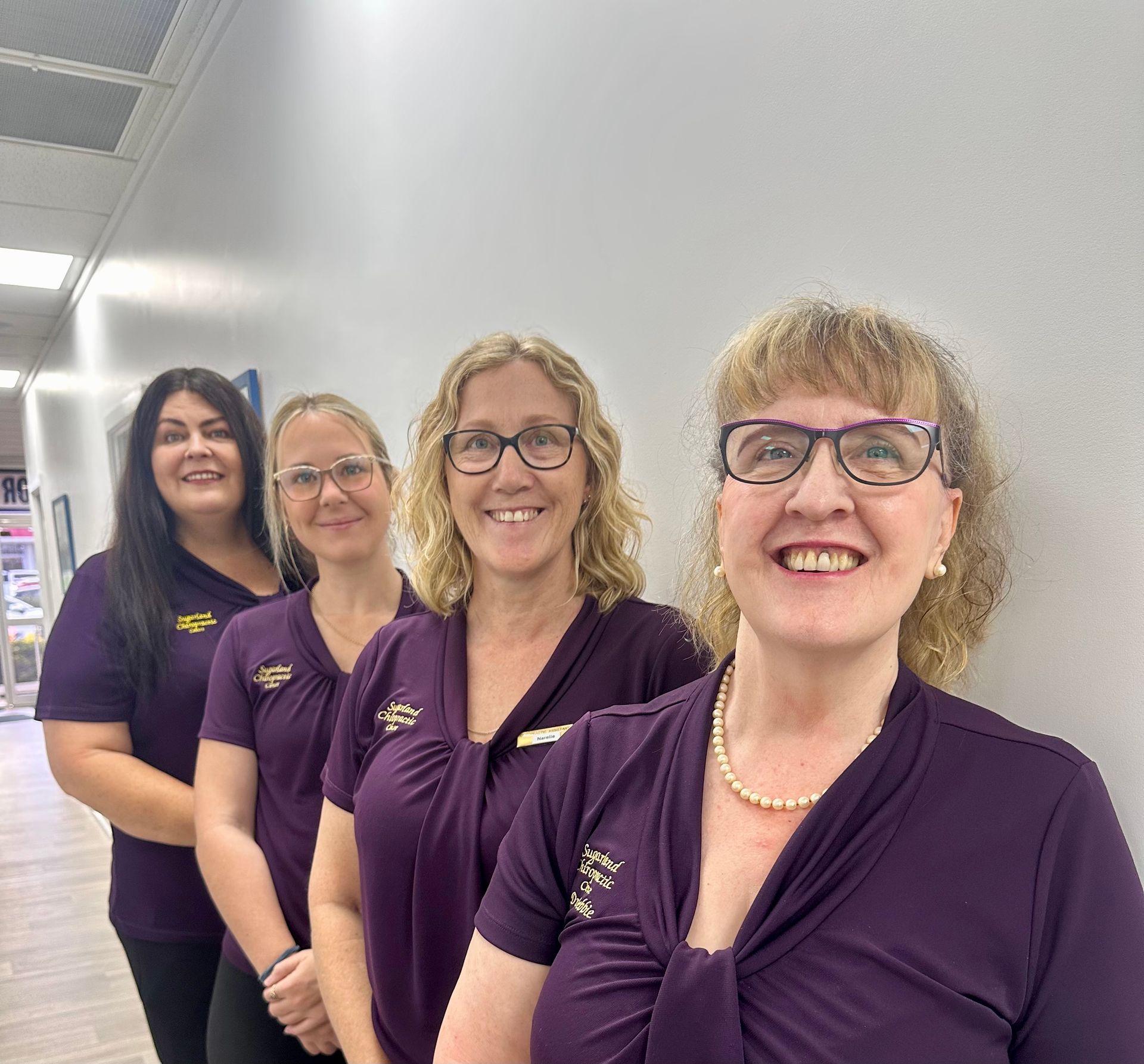 A Group of Women in Purple Shirts Are Standing Next to Each Other in a Hallway — Sugarland Chiropractic Centre in Avoca, QLD