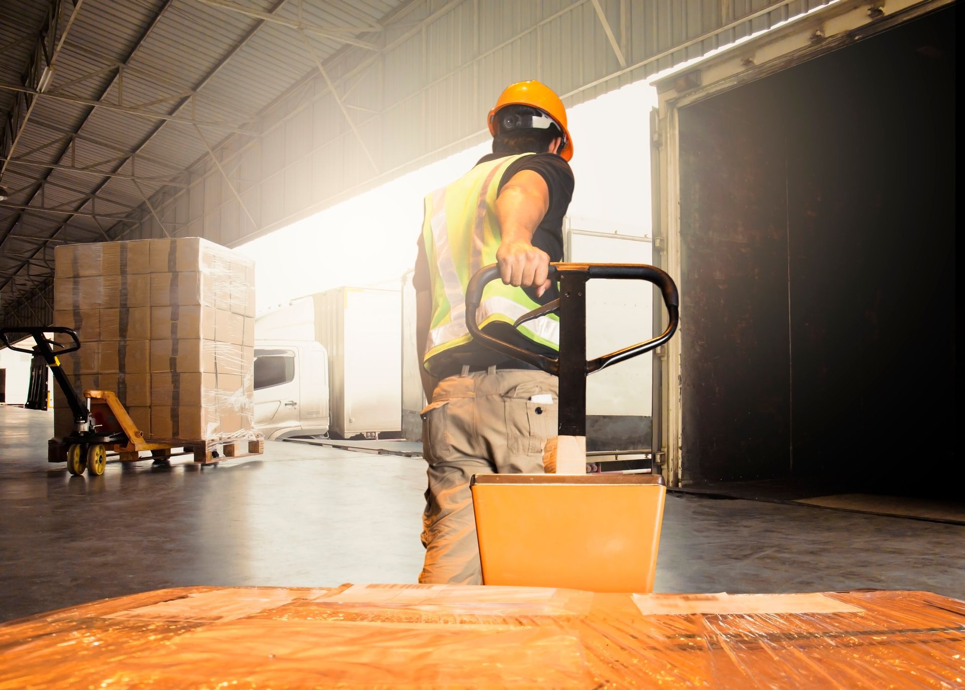 A man is pushing a pallet truck in a warehouse.