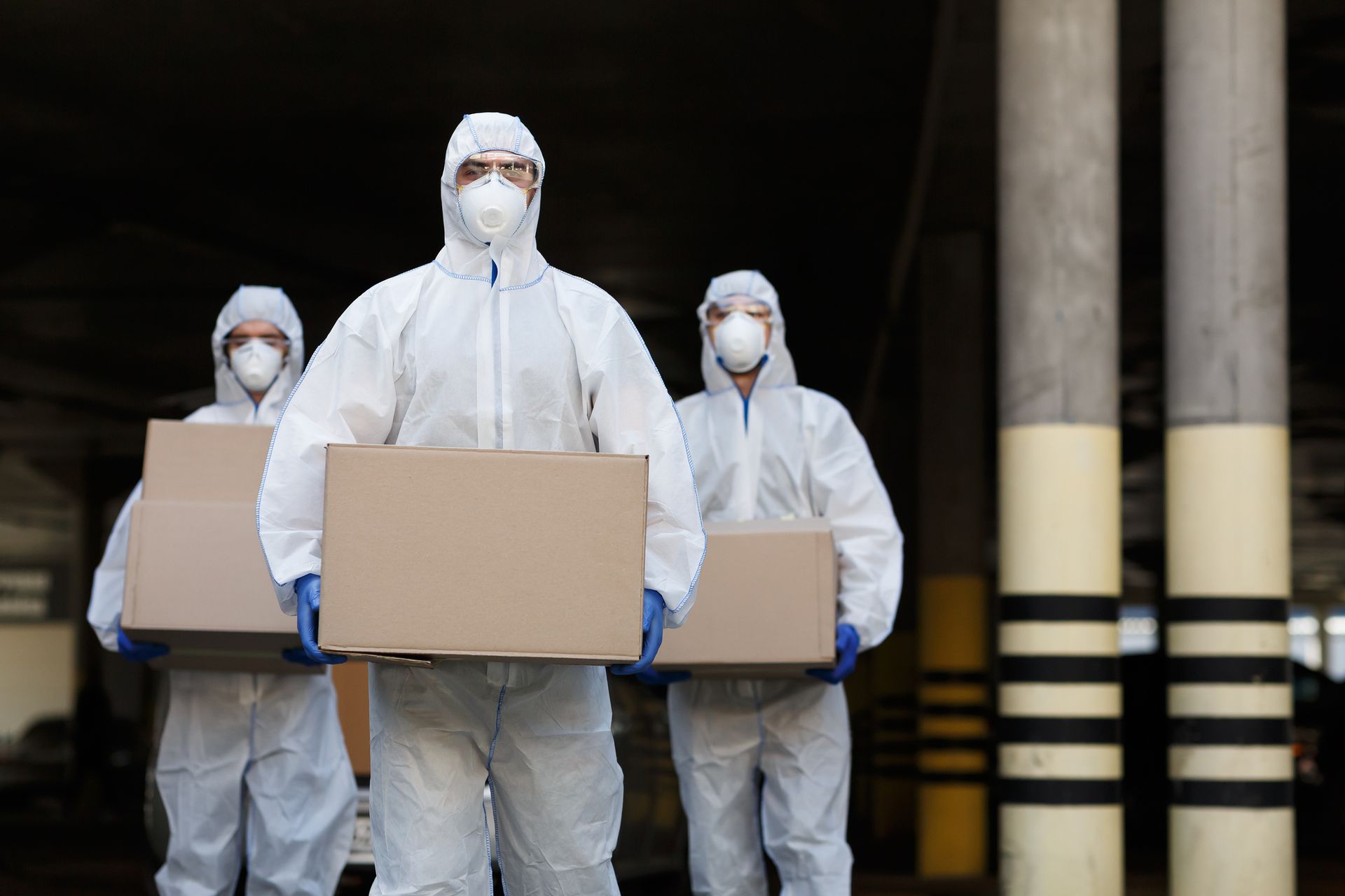 A group of people wearing protective suits and masks are carrying boxes.