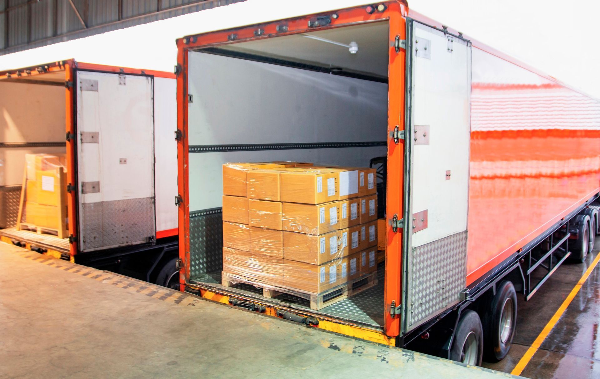 Two semi trucks are parked next to each other in a warehouse.
