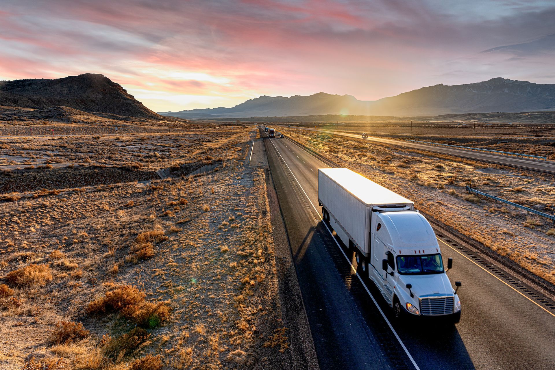 An aerial view of a semi truck driving down a desert highway at sunset.