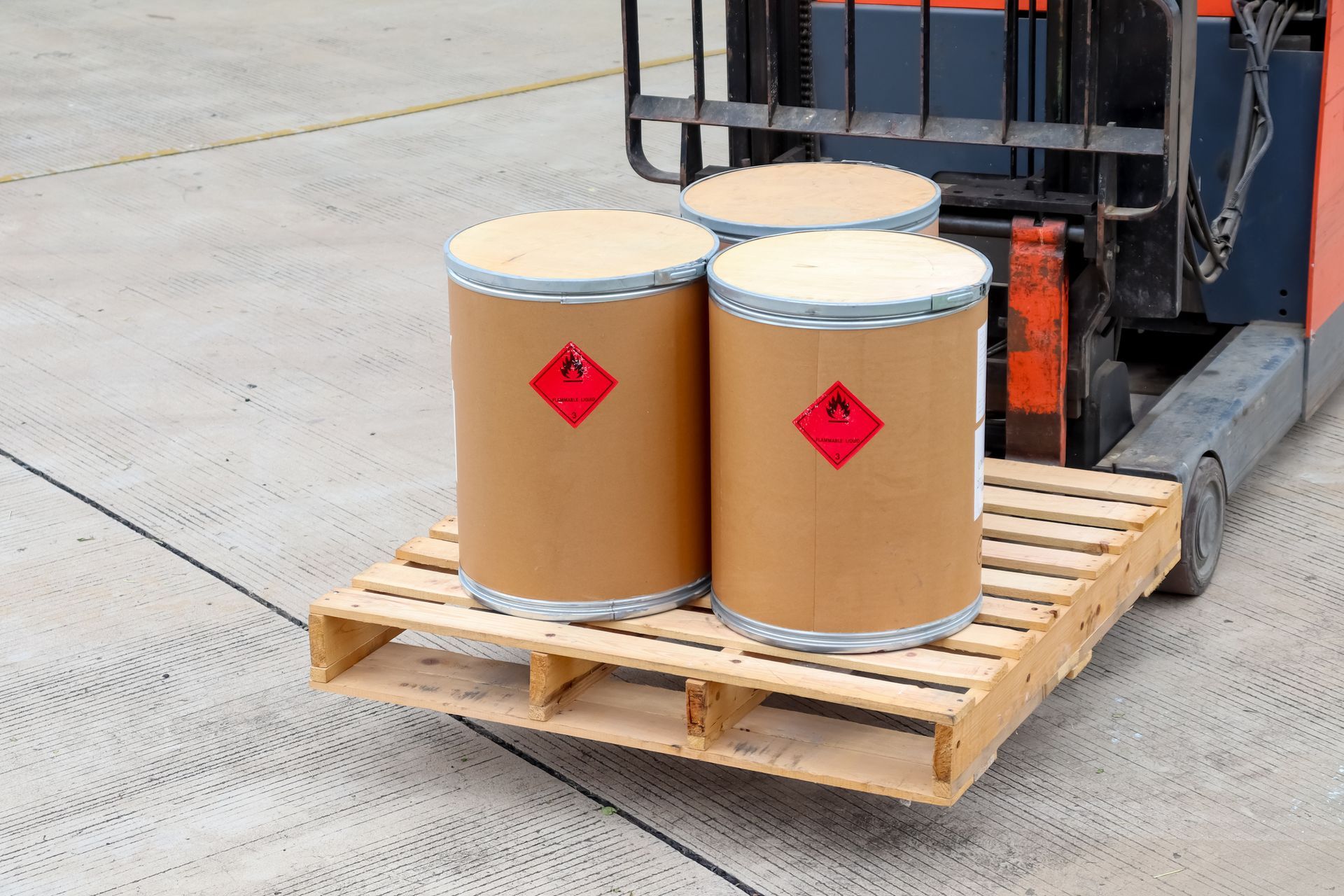 A forklift is carrying three cardboard barrels on a wooden pallet.