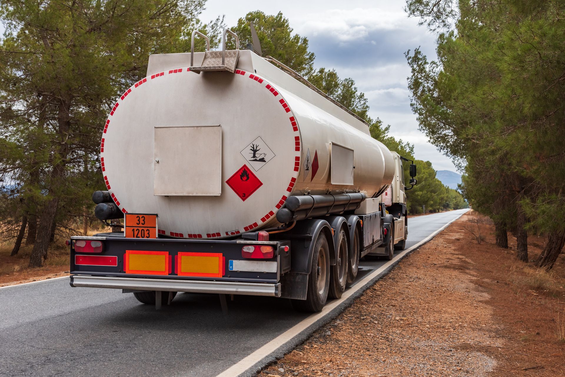 A tanker truck is driving down a road next to trees.