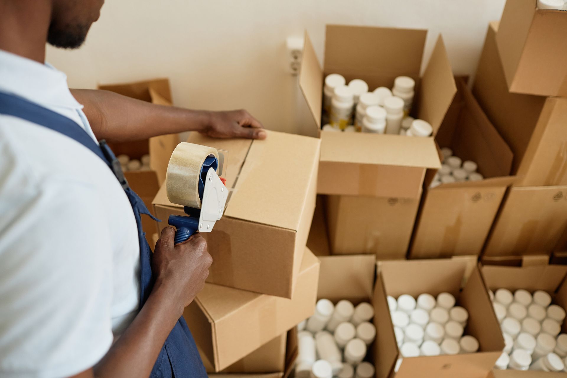 A man is taping a cardboard box with a tape dispenser.