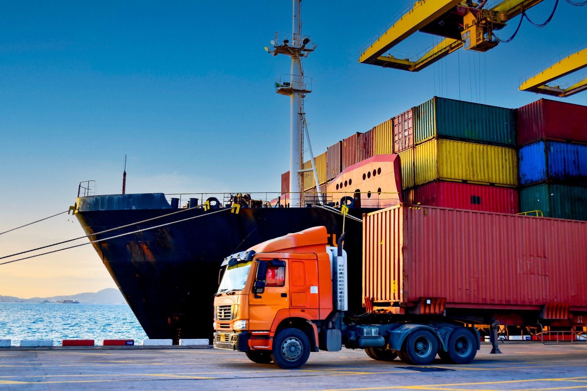 A truck is parked in front of a large ship in a harbor.
