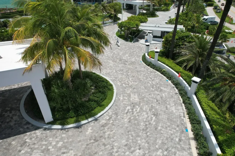 Palm tree-lined driveway with stone pavers, white walls, and lush greenery.