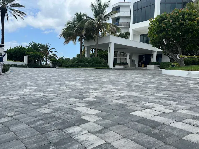 Paved driveway leads to a white building entrance with a canopy. Palm trees and blue sky in the background.