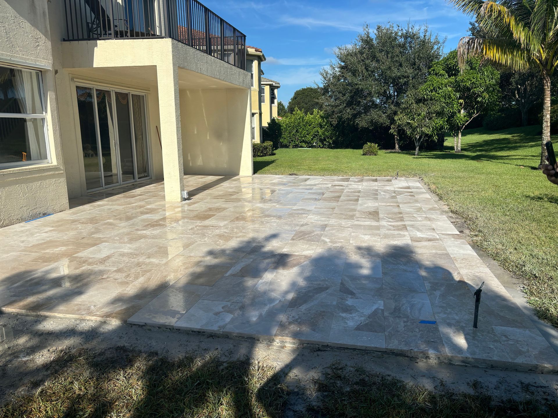 Beige stone patio next to a house with sliding glass doors, surrounded by green grass.