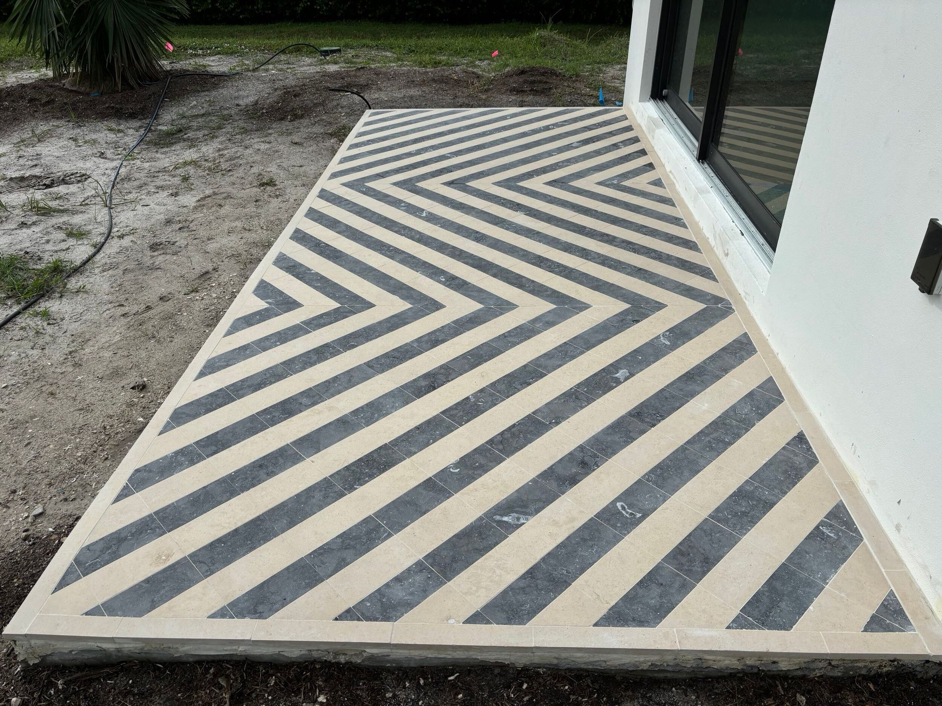 Concrete patio with a black and light gray chevron design next to a white building.