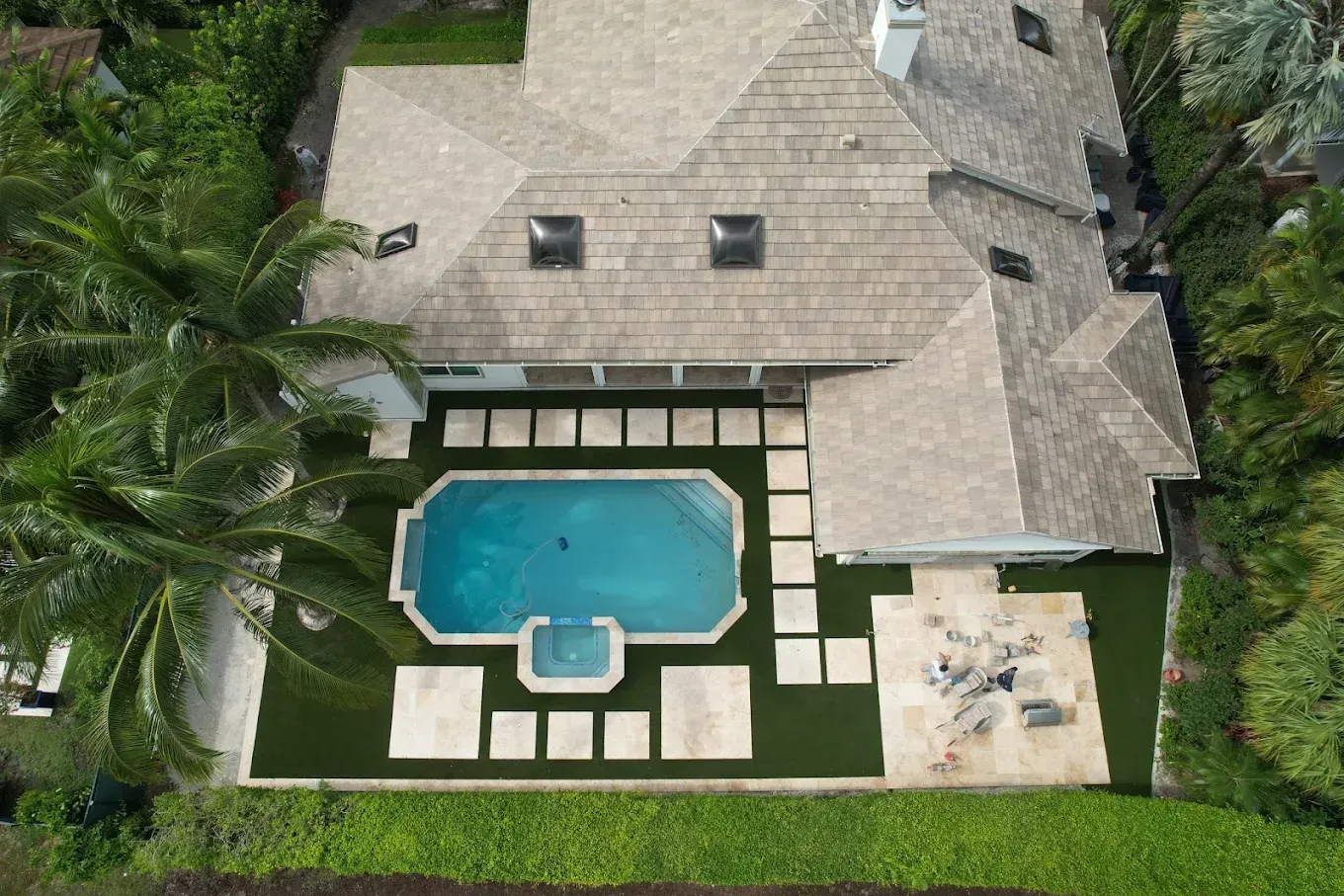 Aerial view of a house with a pool, surrounded by greenery and square stone pavers.