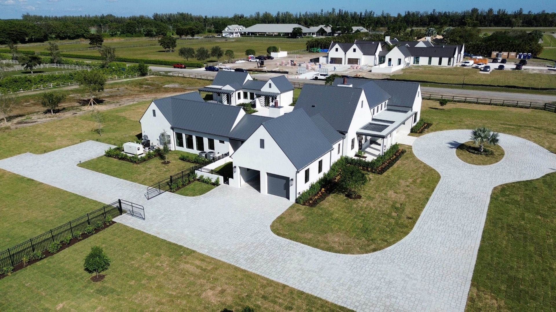 Aerial view of a white modern house with a gray roof and circular driveway on a grassy field.