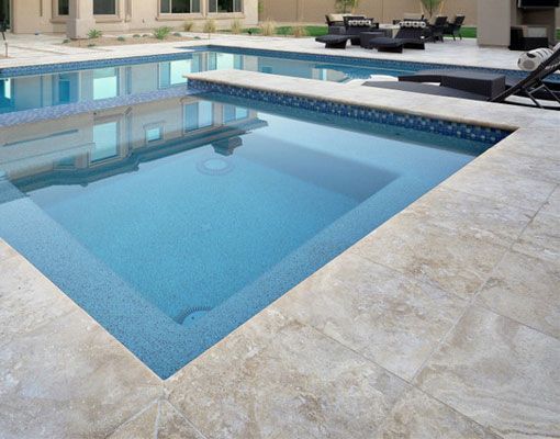 Outdoor swimming pool with blue mosaic tile and beige stone patio.