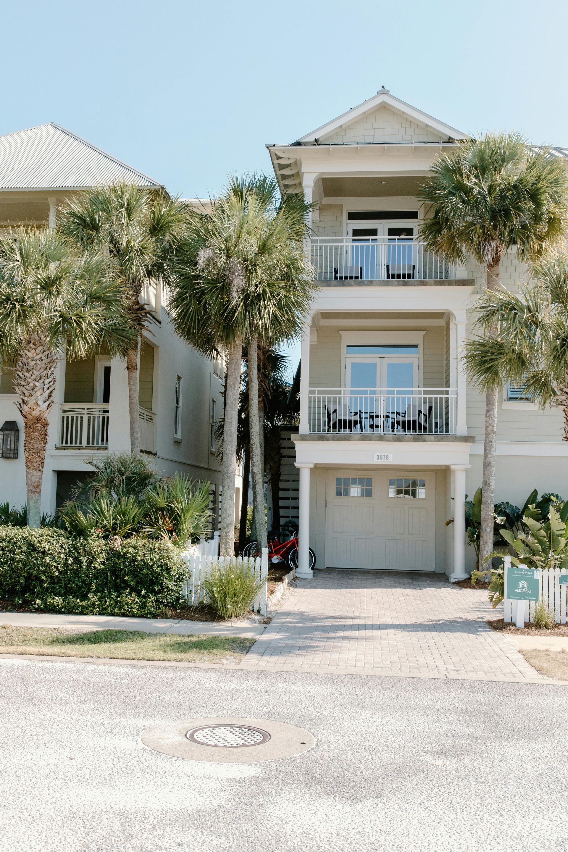 Two-story beach house with white trim and balconies, palm trees in front, blue sky above.