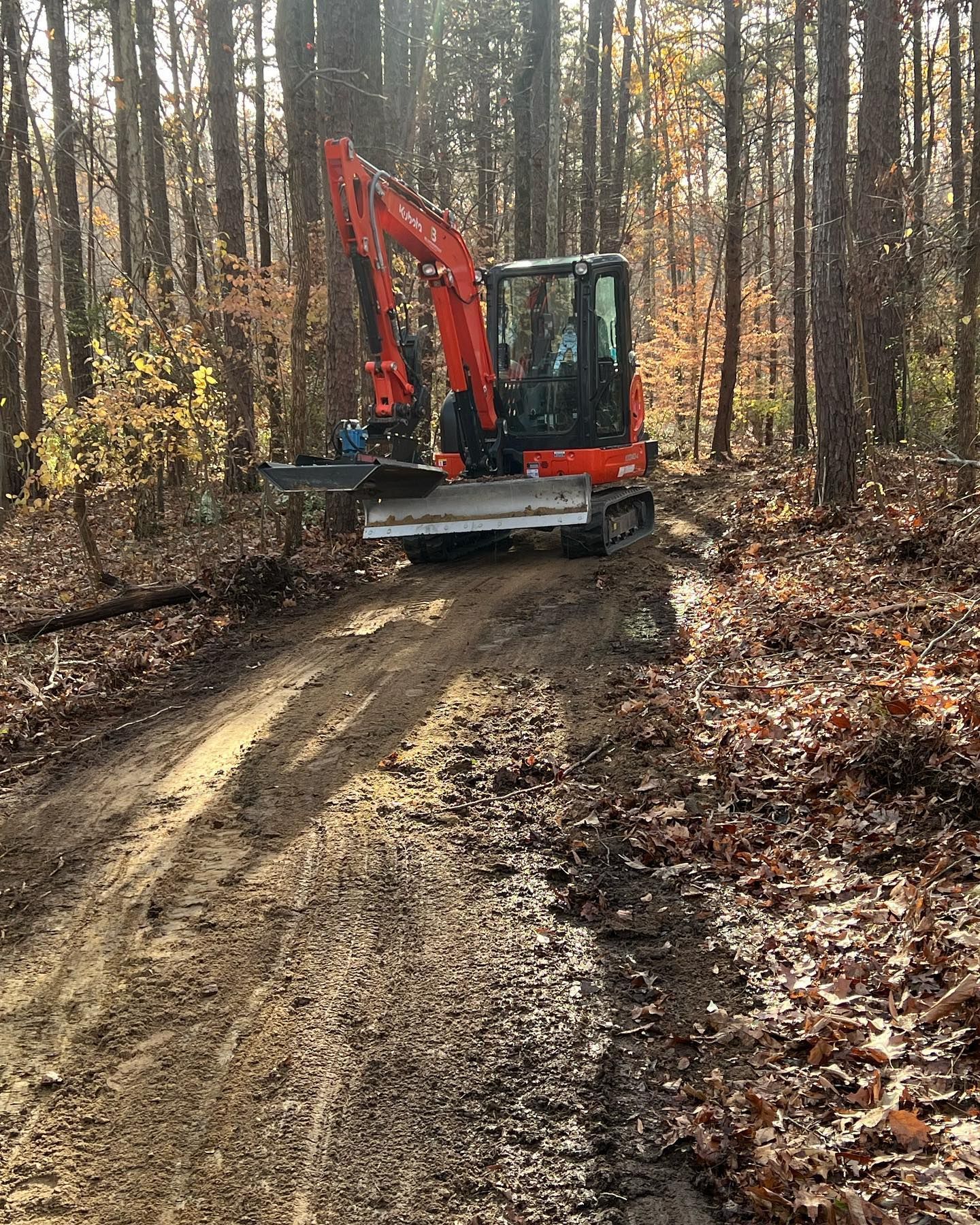 An excavator is driving down a dirt road in the woods.