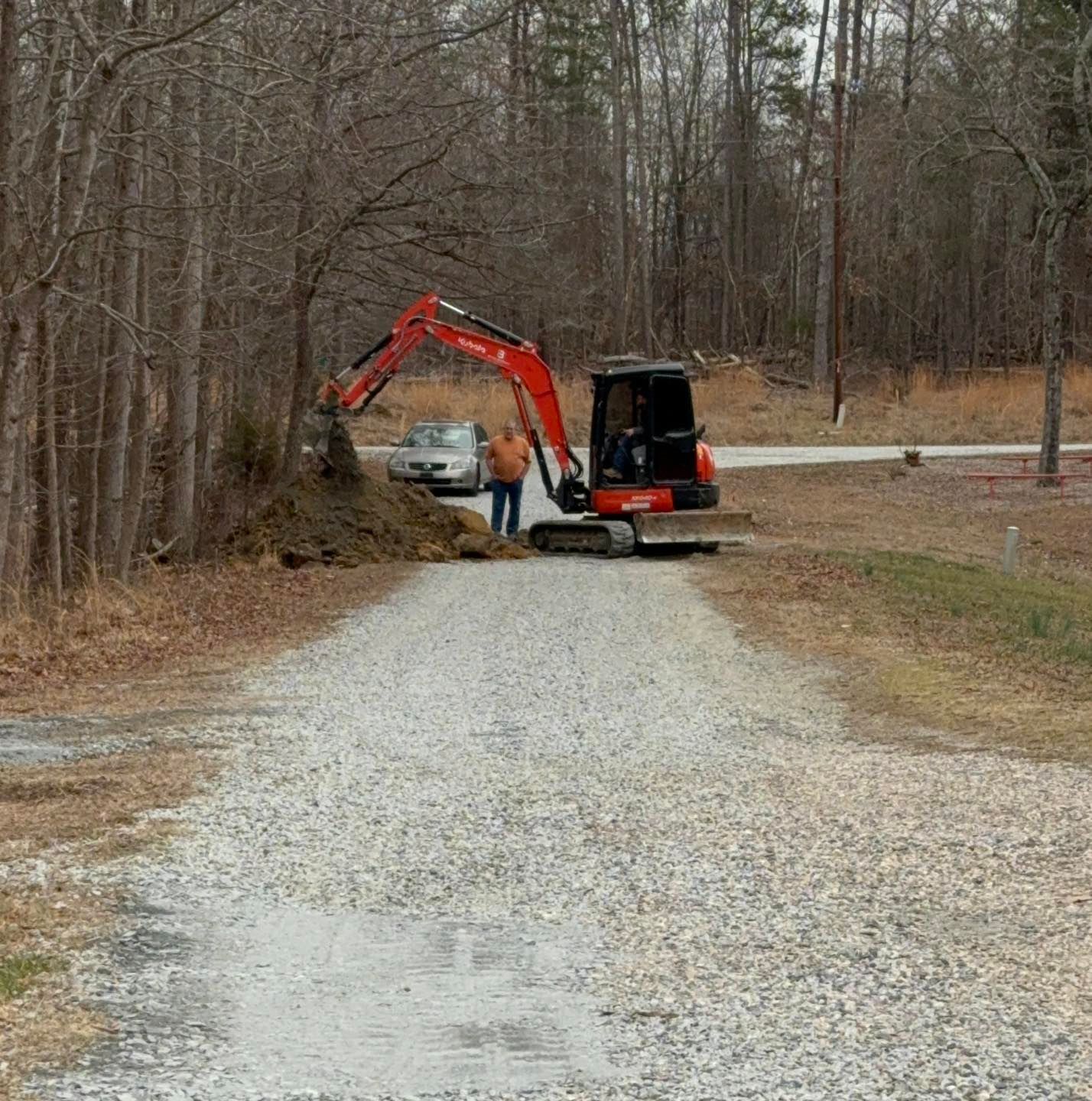 A man is standing next to an excavator on a gravel road.