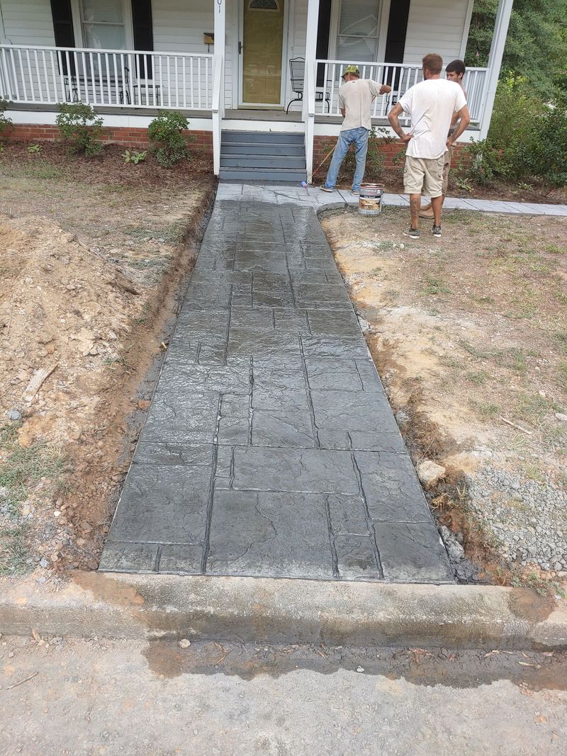 Freshly poured concrete walkway leading to a front porch, with two people standing near the steps.