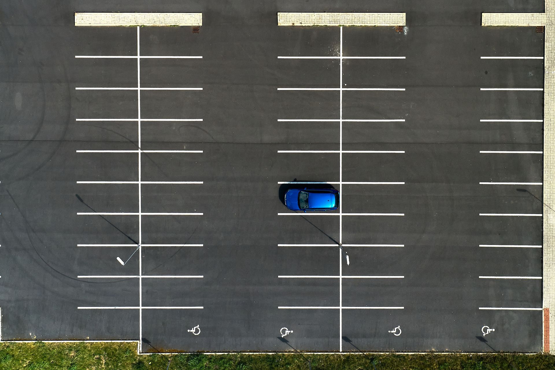 Blue car parked in an empty striped parking lot, viewed from above.
