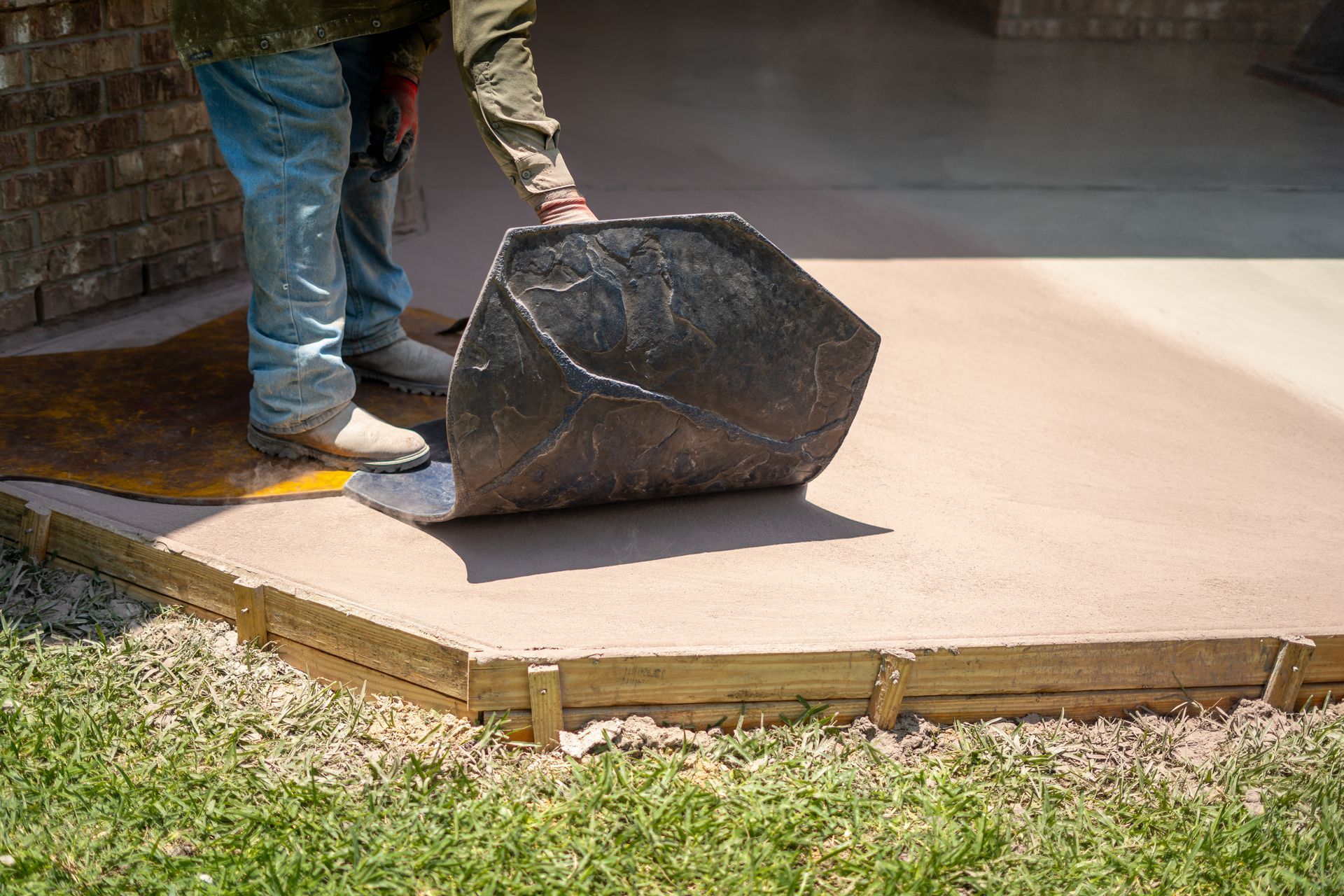 Worker smoothing a fresh concrete slab with a trowel tool outdoors