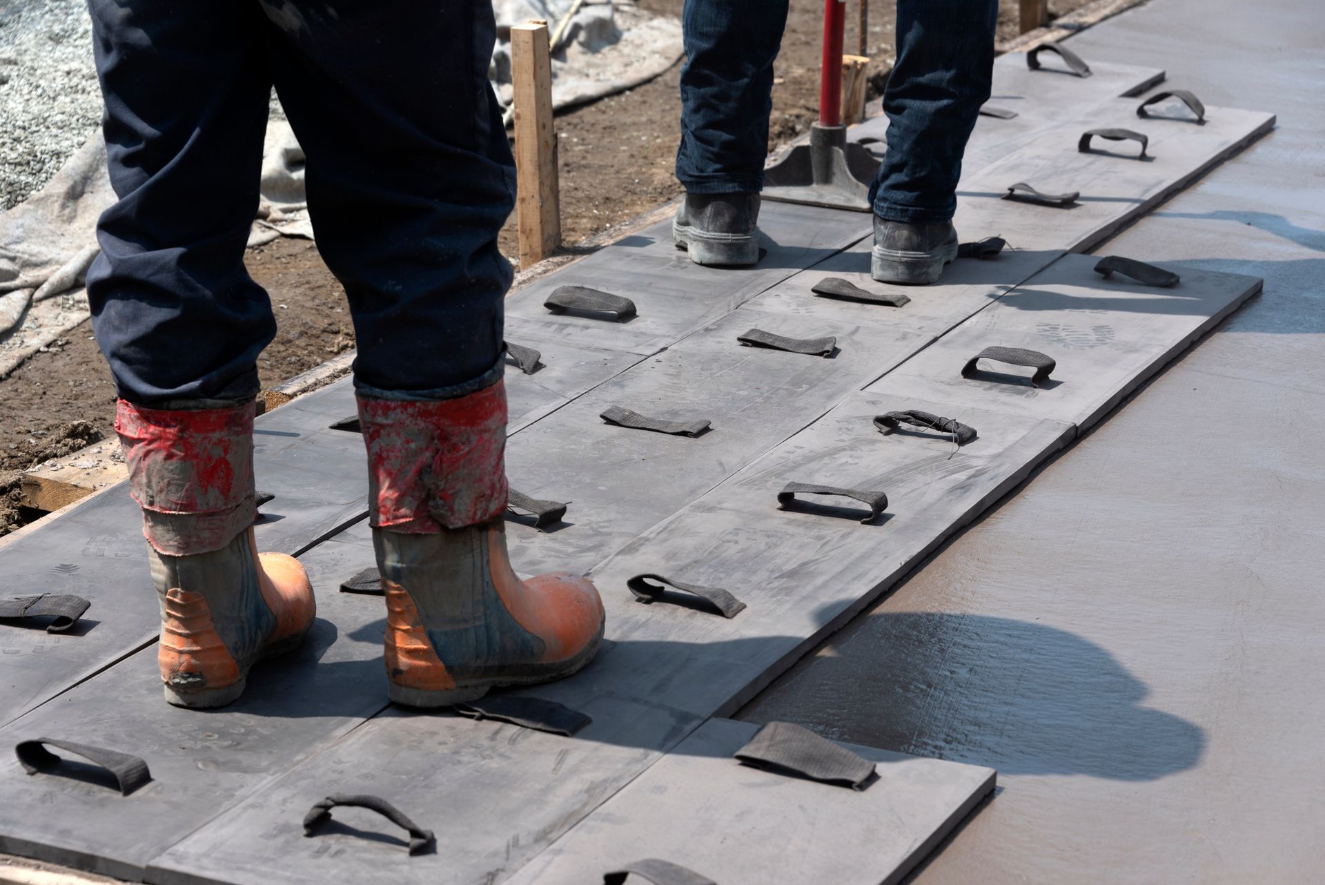 Workers standing on wet concrete placing black formwork panels with handles