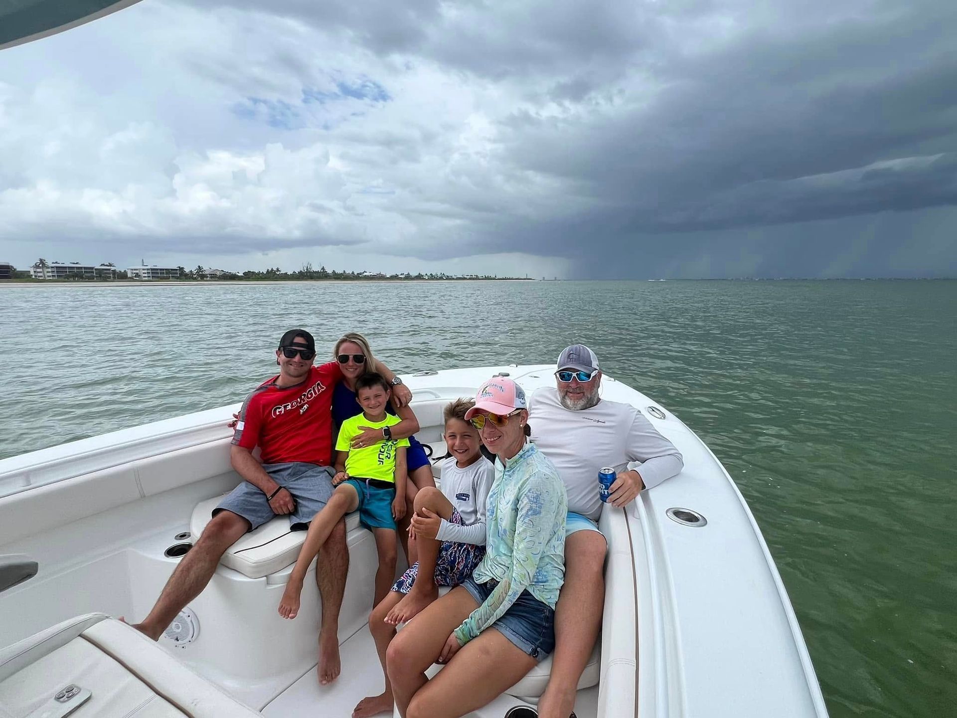 Family on a boat at sea, cloudy sky, sun, smiles, enjoying a coastal trip, water.