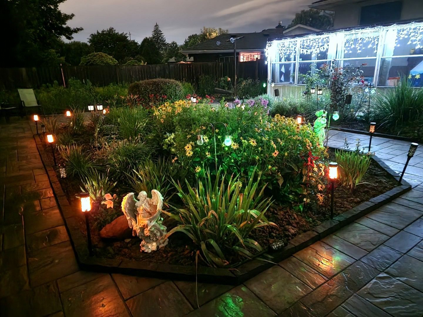 A garden is lit up at night with a house in the background.