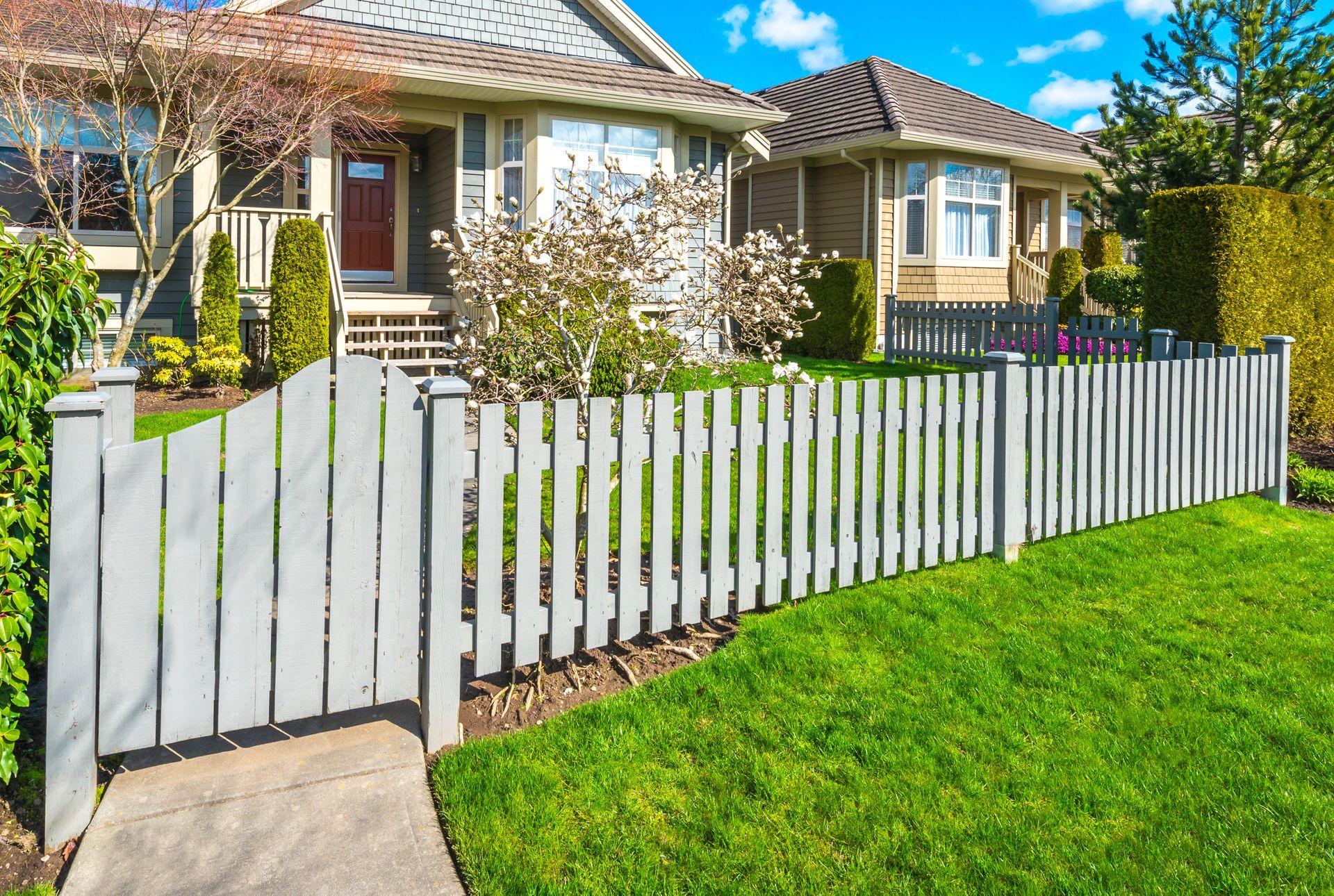 A white picket fence surrounds a lush green lawn in front of a house.