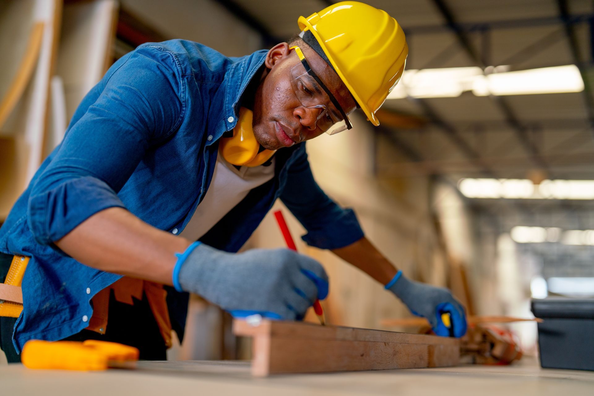 A man wearing a hard hat and safety glasses is measuring a piece of wood.