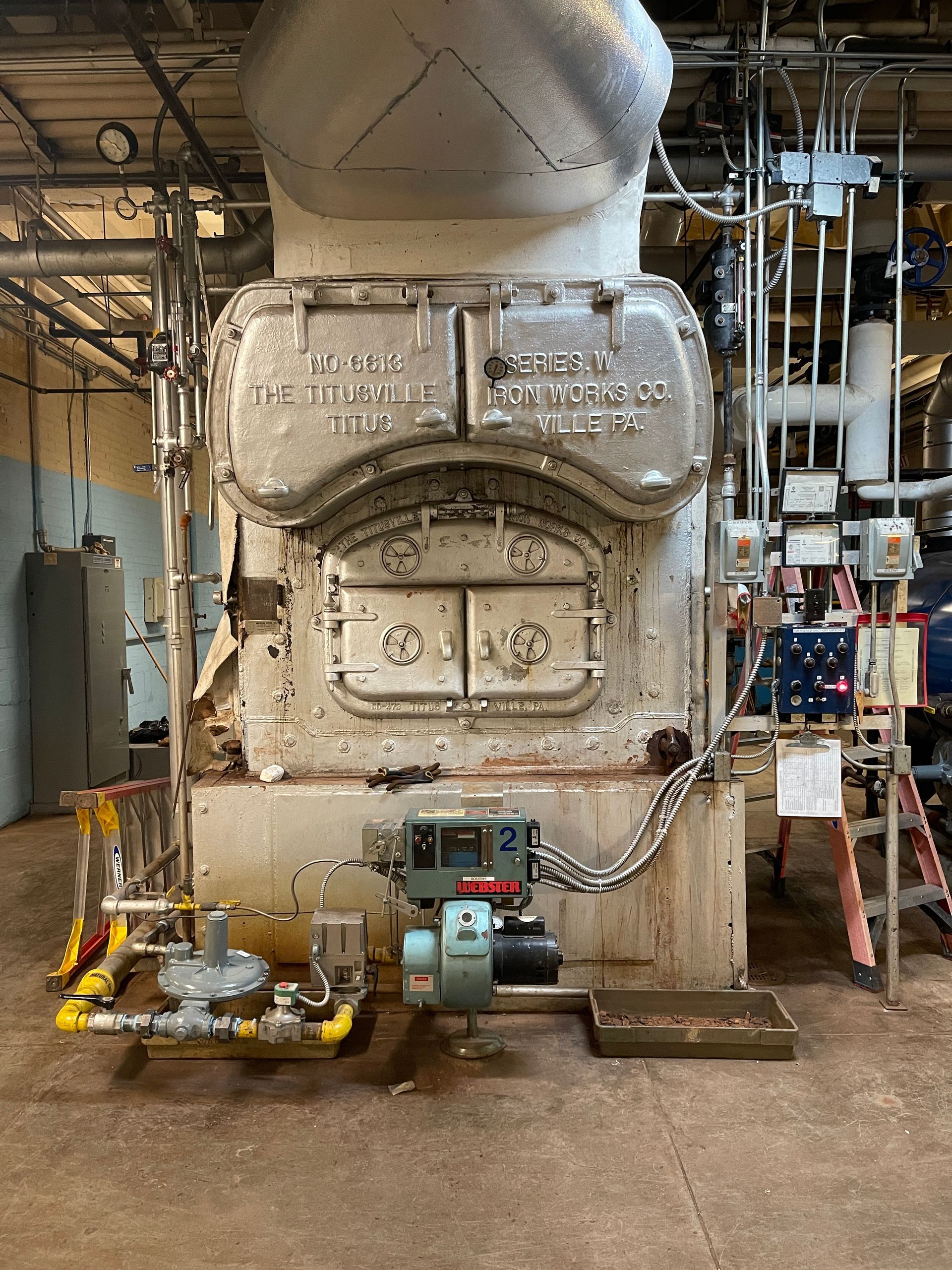 A large boiler is sitting in a room with pipes.