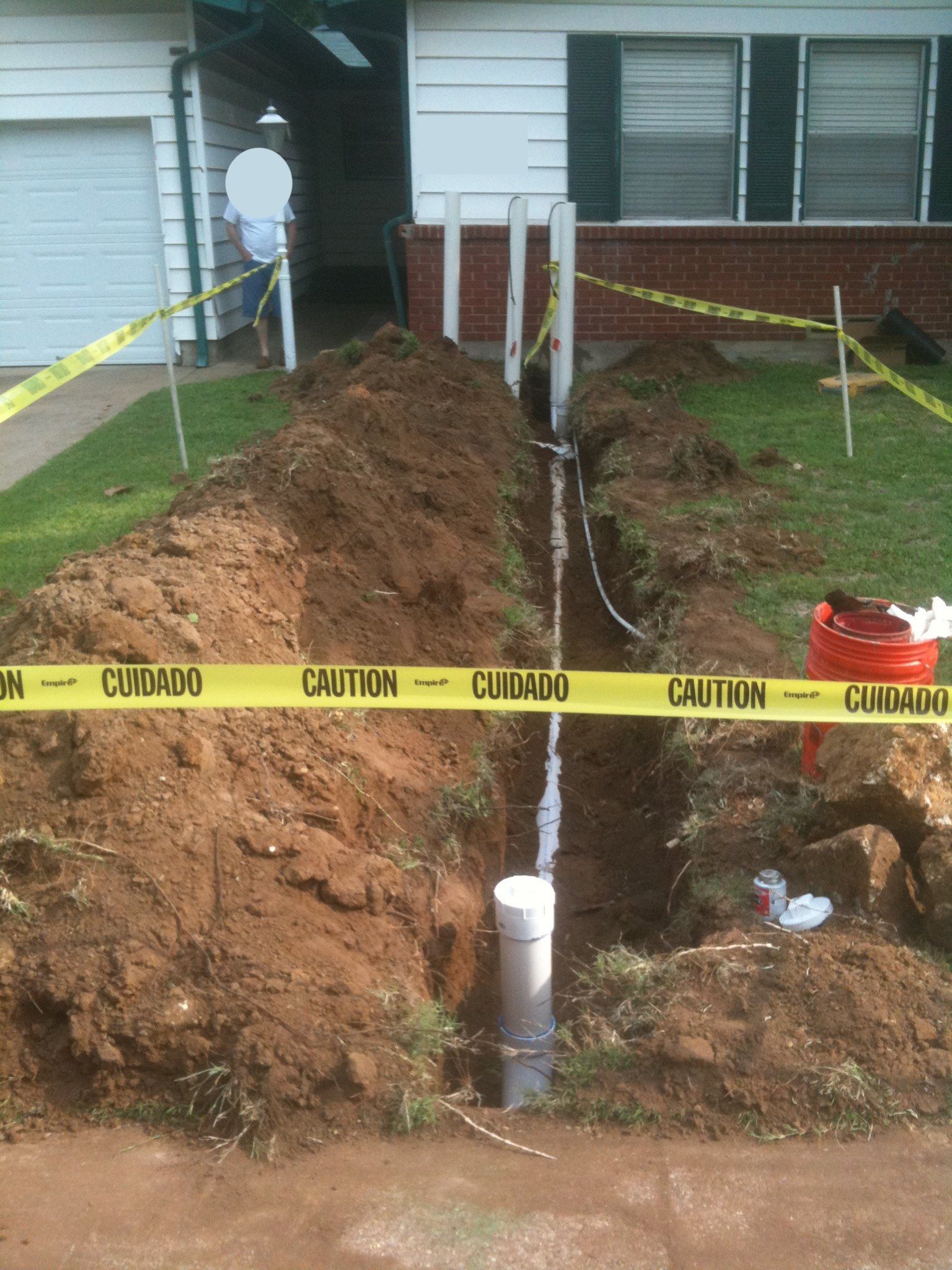 Calhoun Plumbing Services LLC | A yellow caution tape surrounds a hole in the ground in front of a house
