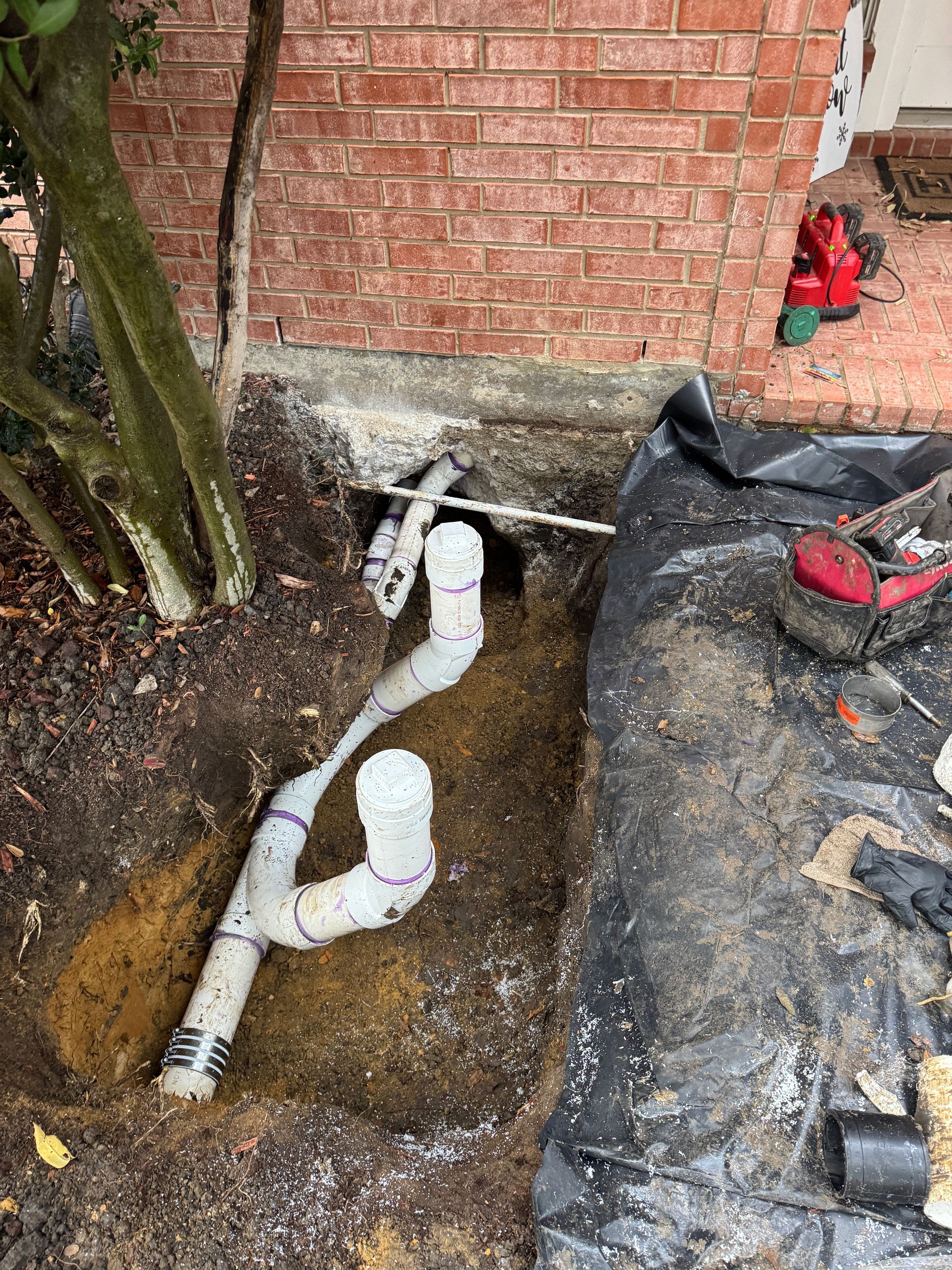 Calhoun Plumbing Services LLC | A drain pipe is being installed in the ground next to a brick wall.