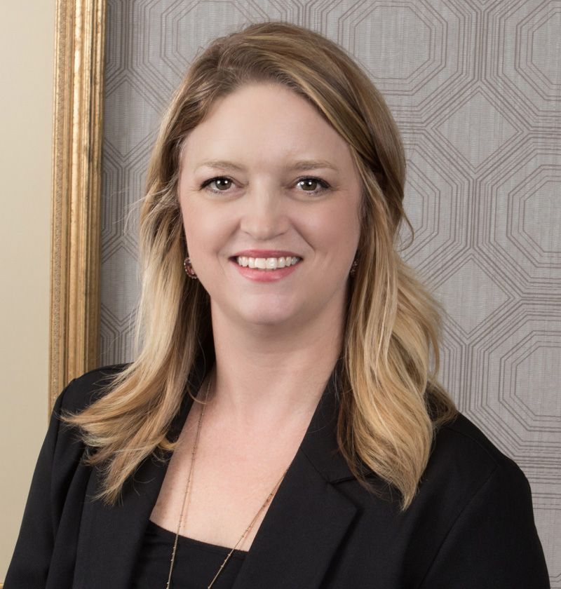 Smiling woman in a black blazer against a patterned wall.