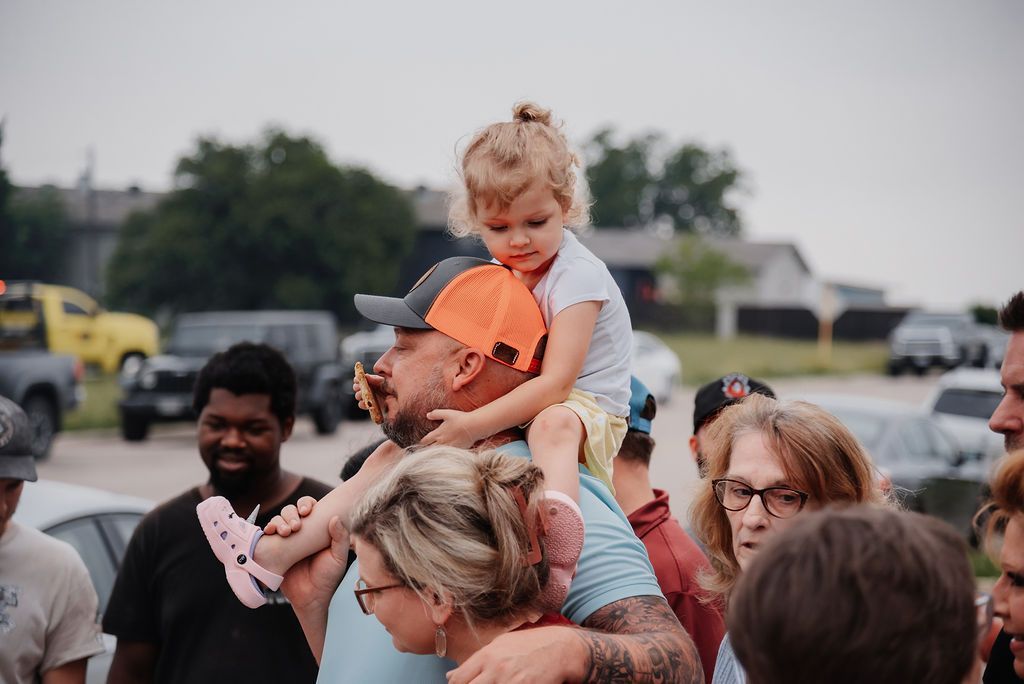 A man is carrying a little girl on his shoulders in a crowd of people. | Chuck's Garage