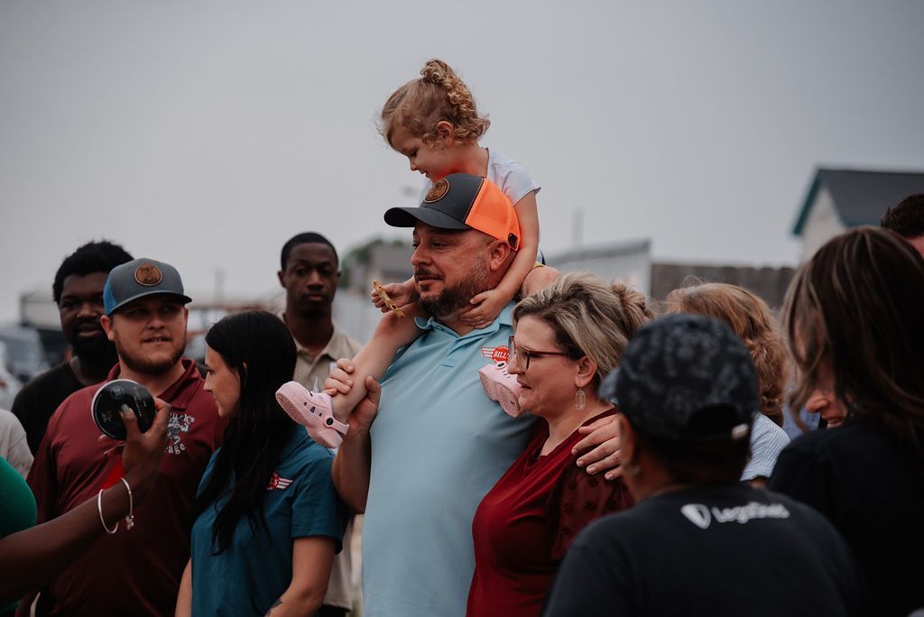 A man is holding a little girl on his shoulders in a crowd of people. | Chuck's Garage
