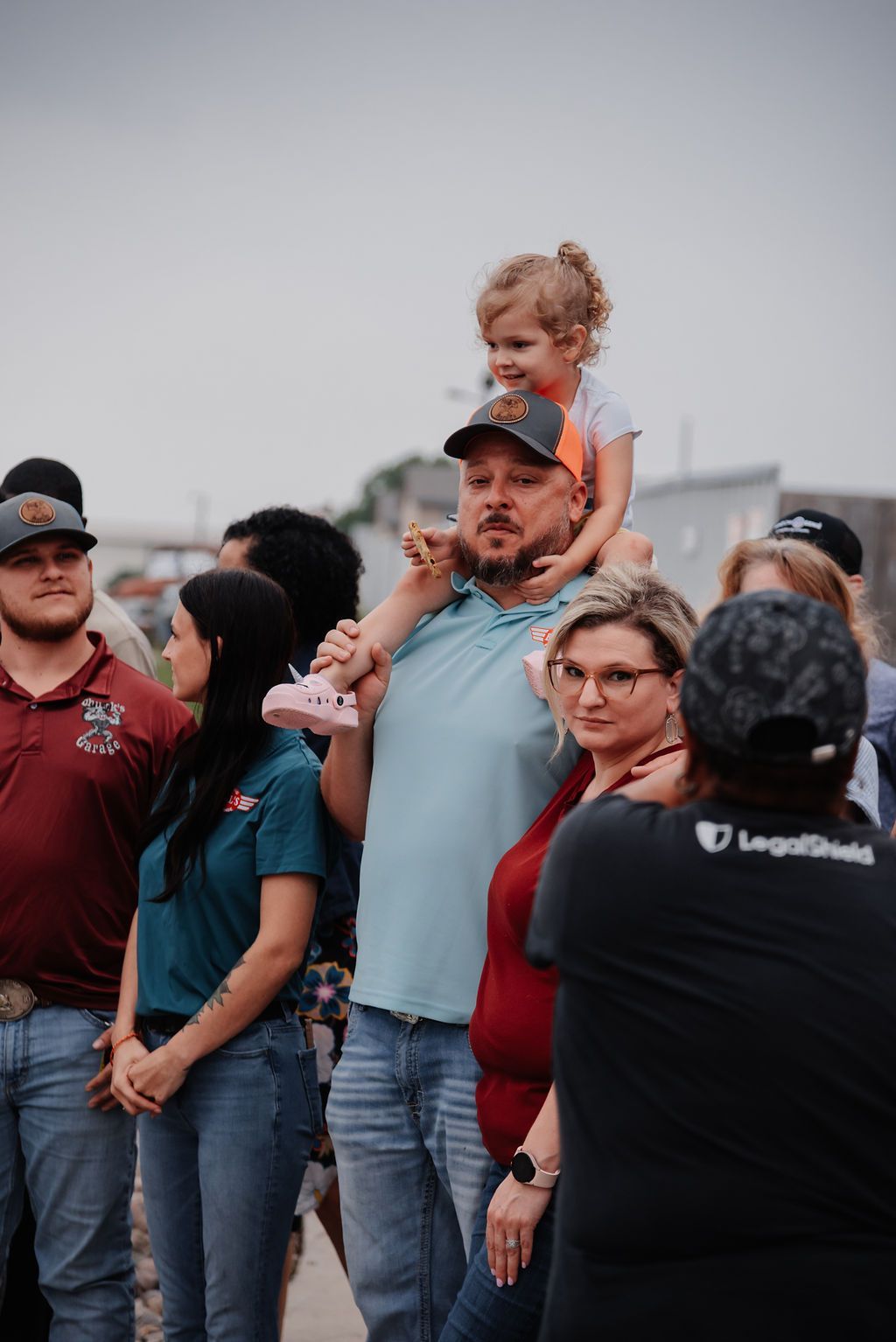 A man is carrying a little girl on his shoulders in a crowd of people. | Chuck's Garage