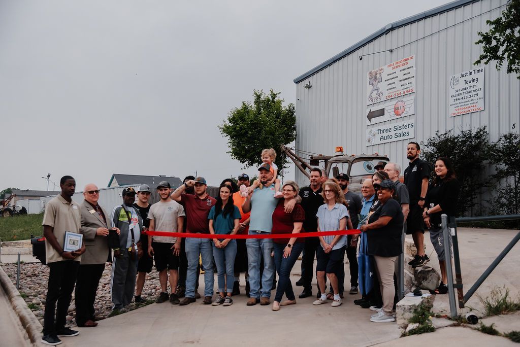A group of people are standing in front of a building holding a red ribbon. | Chuck's Garage