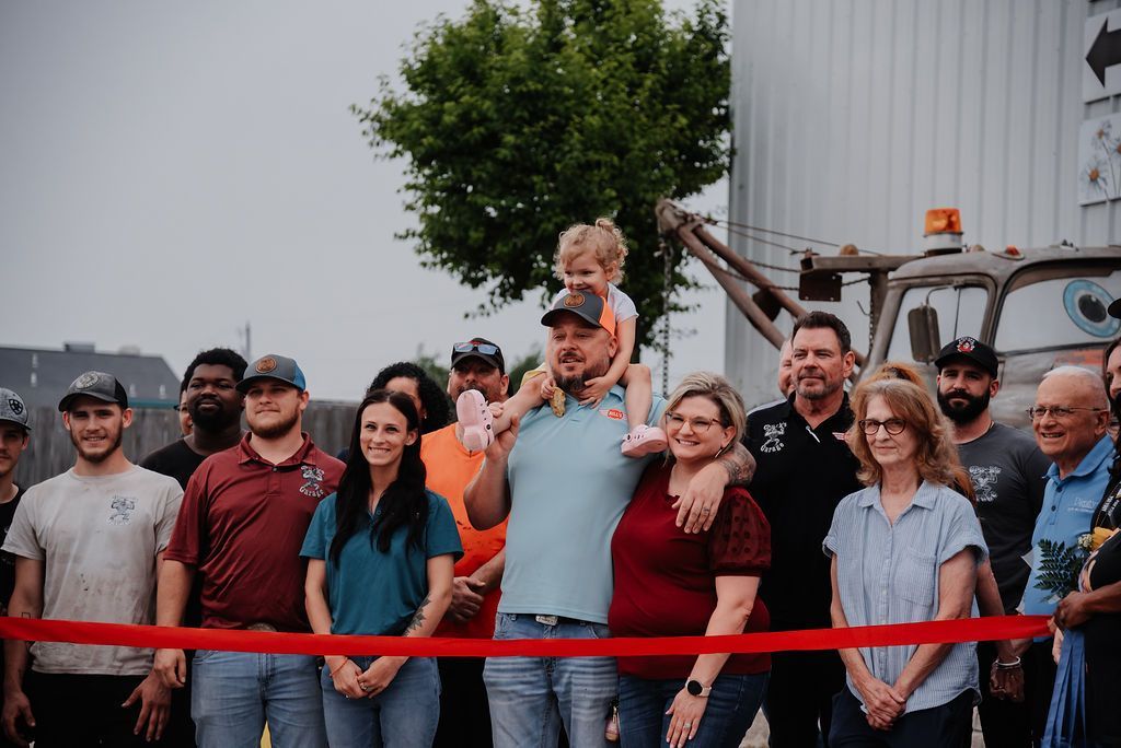 A group of people are standing in front of a red ribbon. | Chuck's Garage