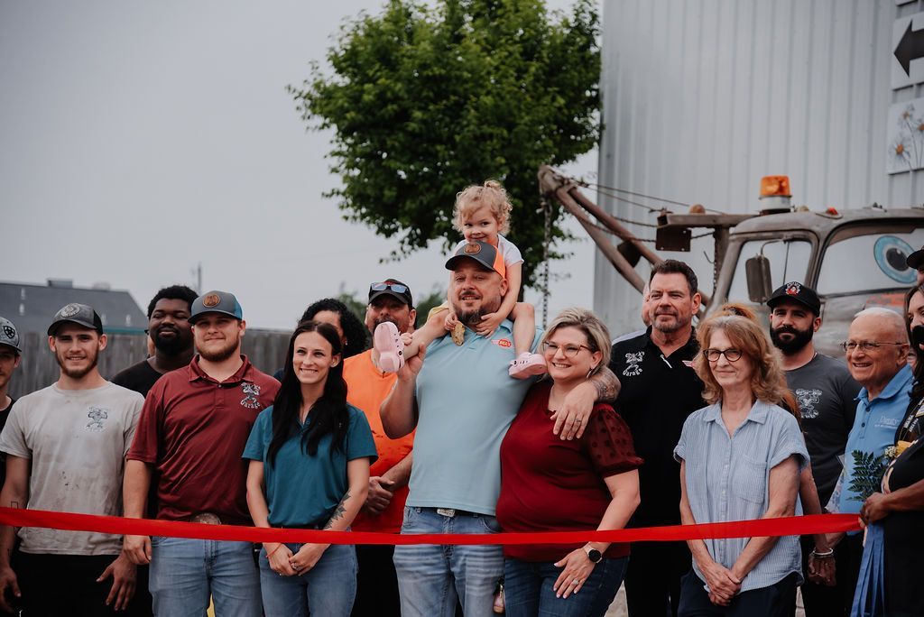 A group of people are standing in front of a red ribbon. | Chuck's Garage