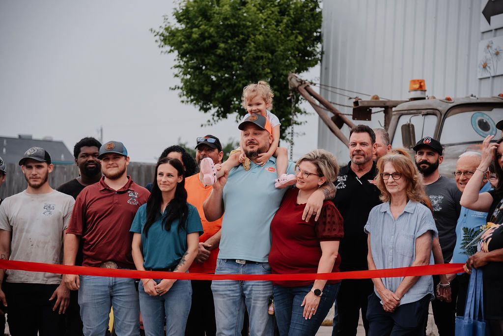 A group of people are standing in front of a red ribbon. | Chuck's Garage