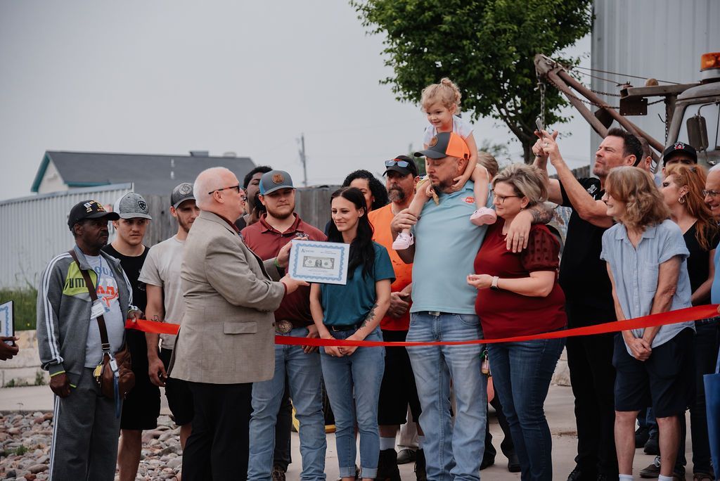 A group of people are standing around a man cutting a red ribbon. | Chuck's Garage