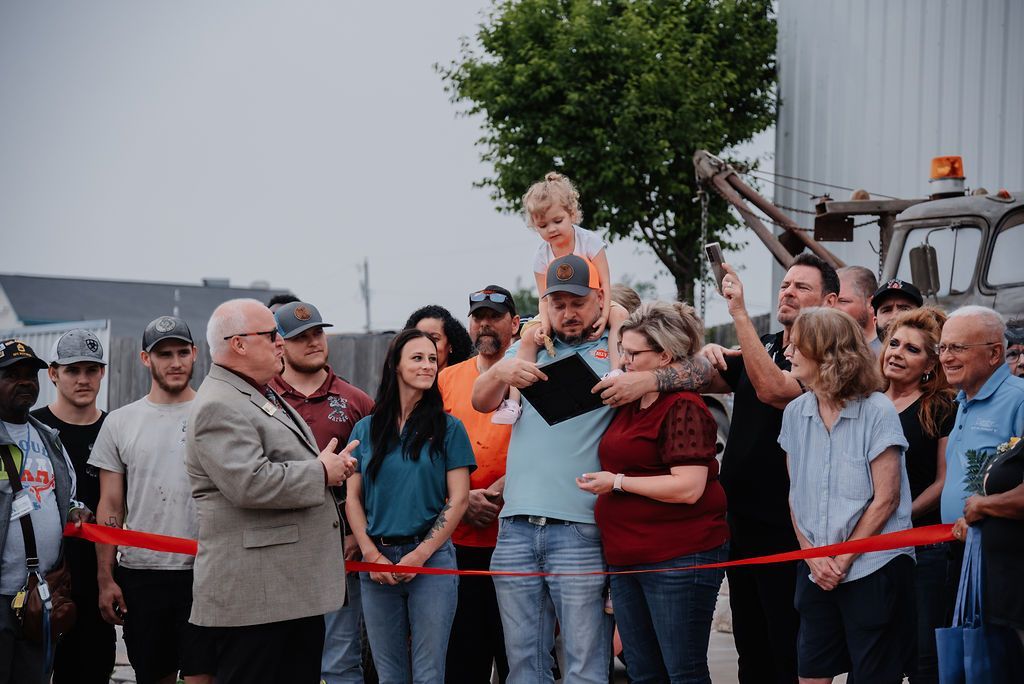 A group of people are standing around a man cutting a red ribbon. | Chuck's Garage