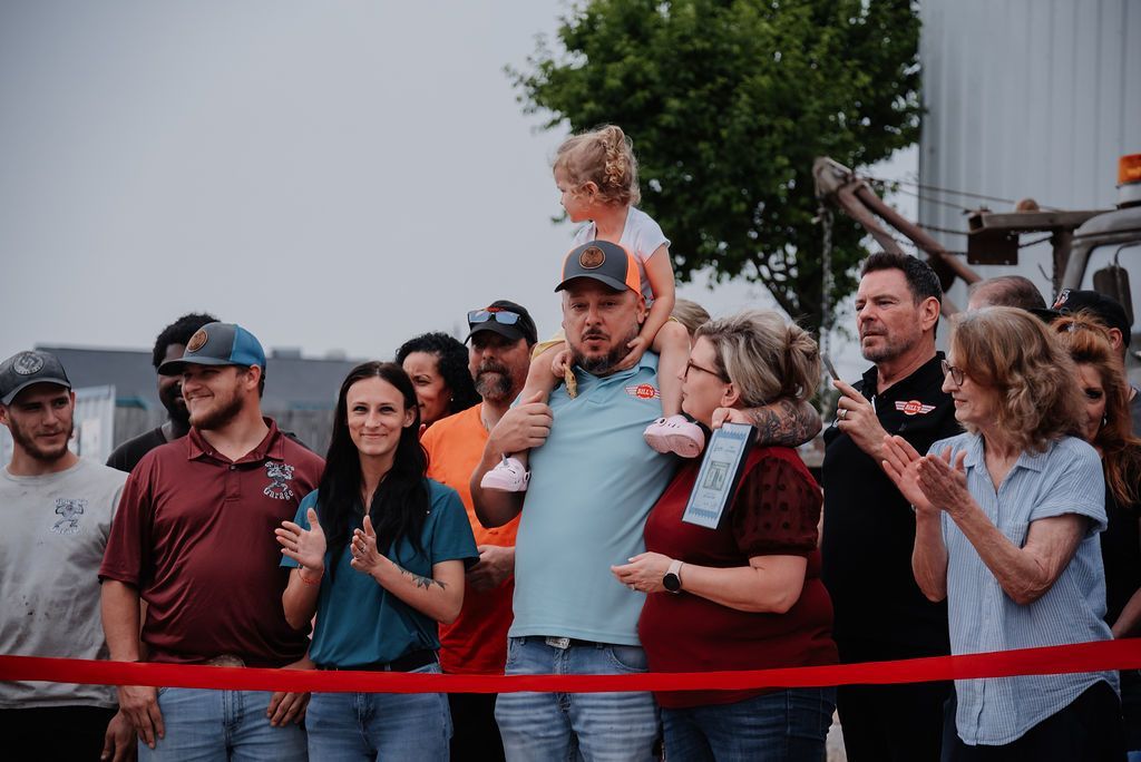 A group of people are standing around a red ribbon. | Chuck's Garage