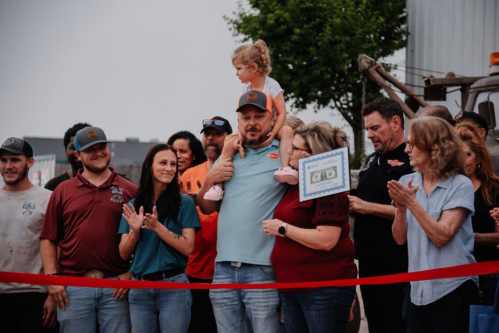 A group of people are standing around a red ribbon. | Chuck's Garage